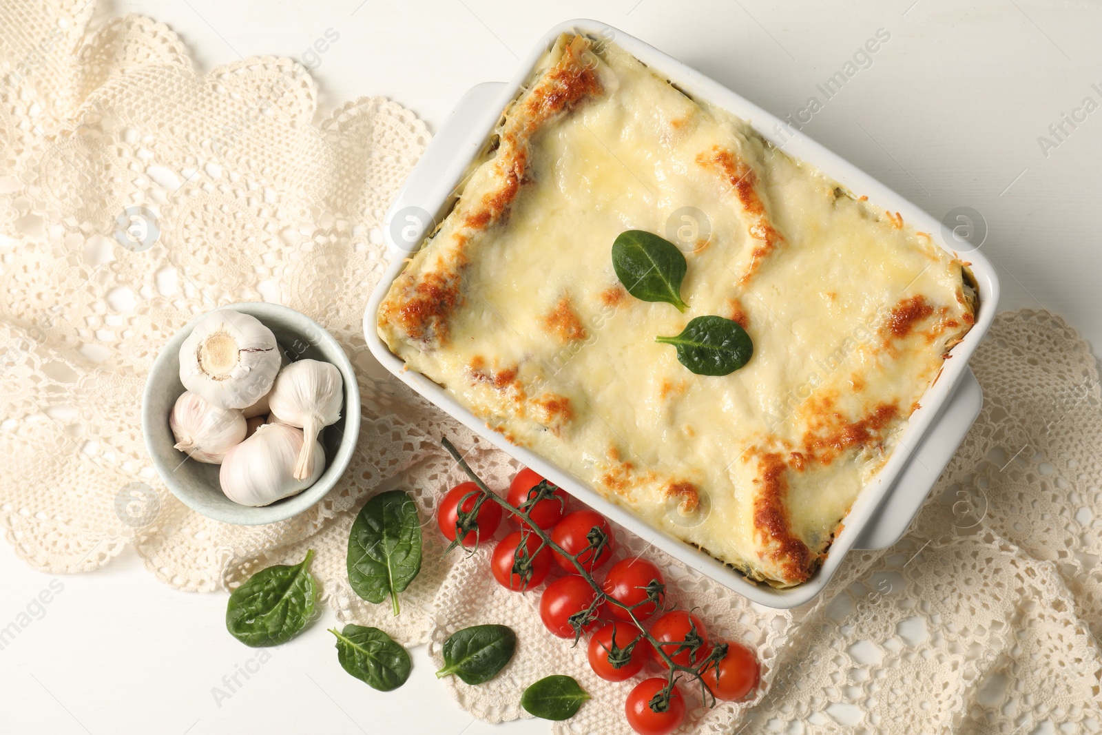 Photo of Delicious spinach lasagna in baking dish and ingredients on white table, flat lay