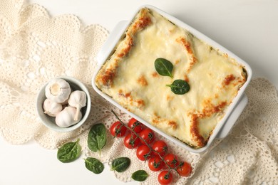 Photo of Delicious spinach lasagna in baking dish and ingredients on white table, flat lay