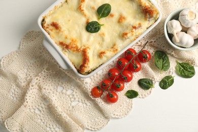 Photo of Delicious spinach lasagna in baking dish and ingredients on white table, flat lay