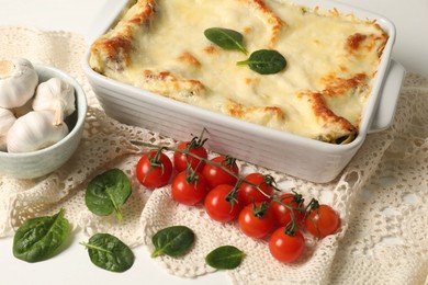 Photo of Delicious spinach lasagna in baking dish and ingredients on white table