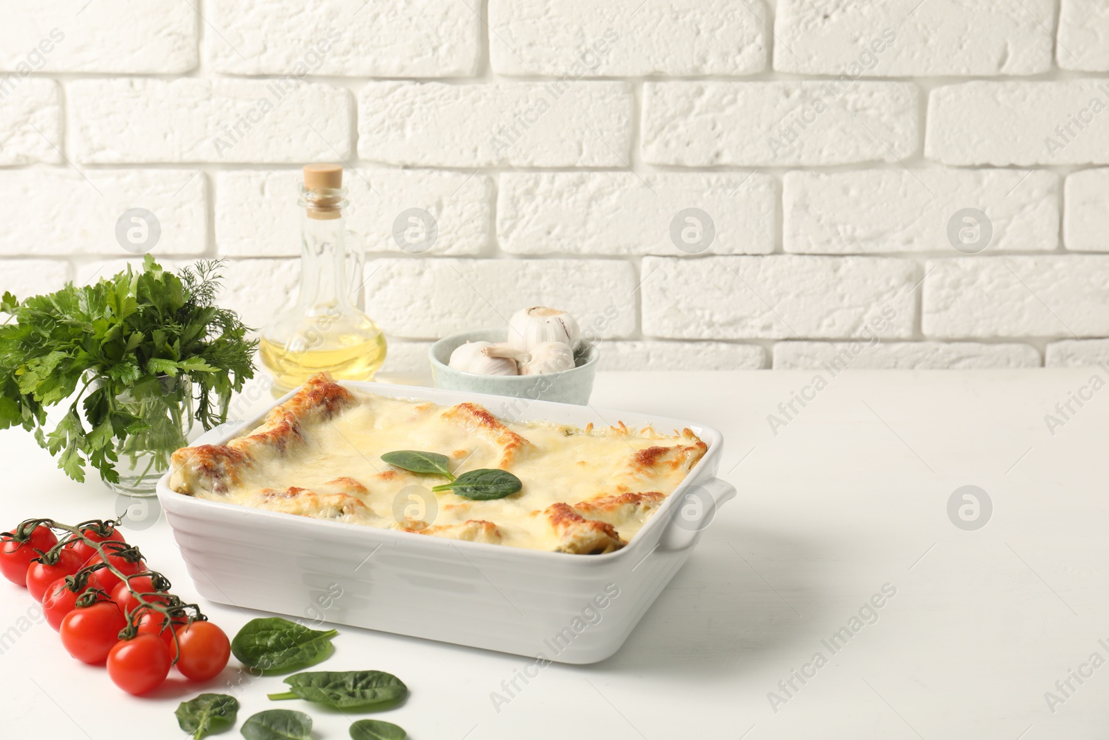 Photo of Delicious spinach lasagna in baking dish and ingredients on white table, space for text