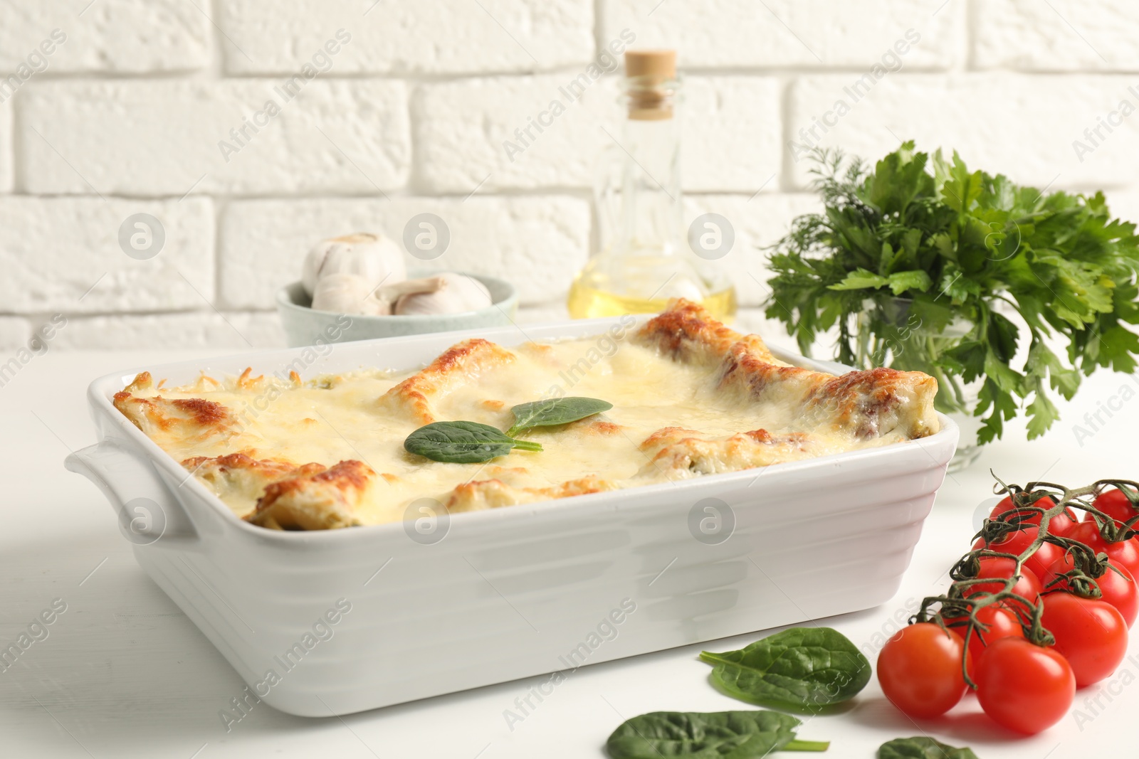 Photo of Delicious spinach lasagna in baking dish and ingredients on white table