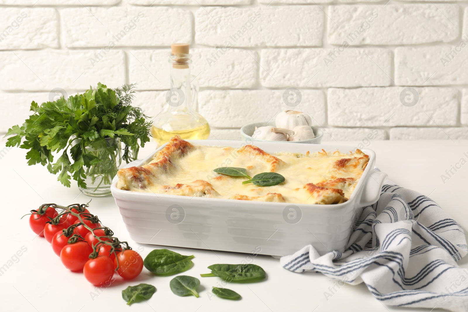 Photo of Delicious spinach lasagna in baking dish and ingredients on white table