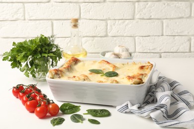 Photo of Delicious spinach lasagna in baking dish and ingredients on white table