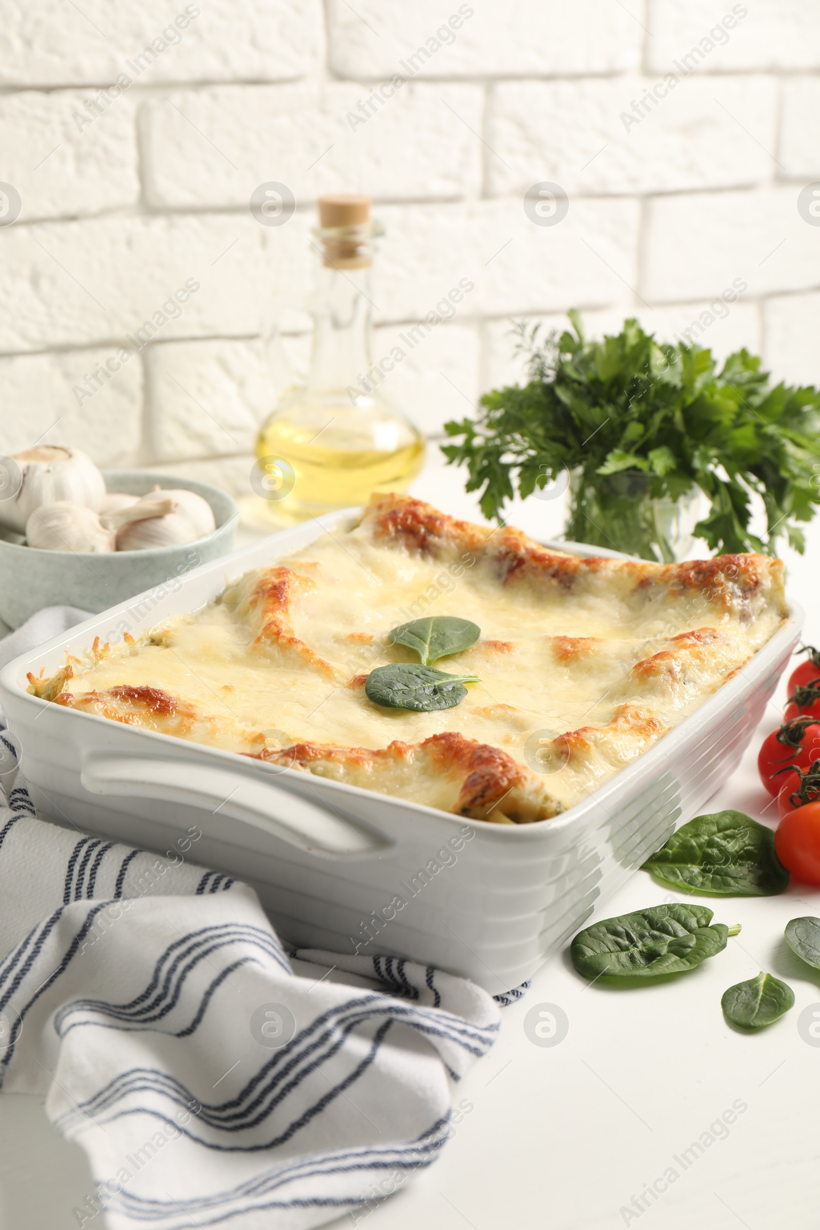 Photo of Delicious spinach lasagna in baking dish and ingredients on white table