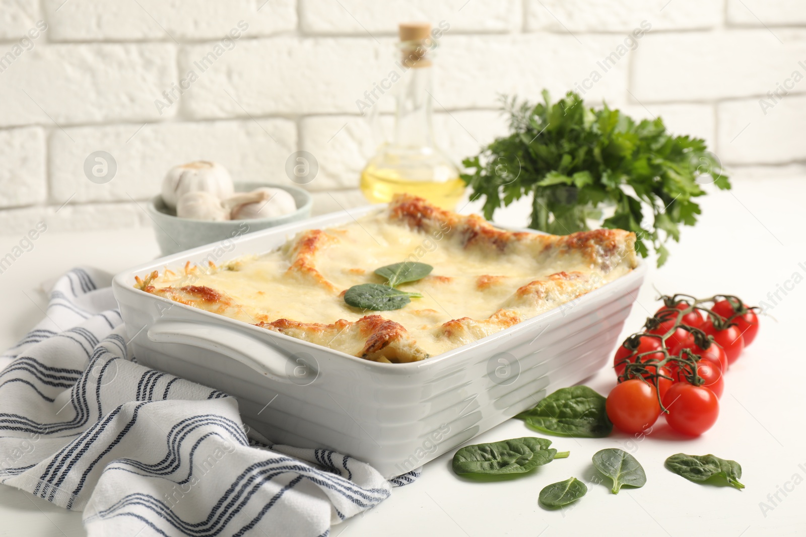 Photo of Delicious spinach lasagna in baking dish and ingredients on white table