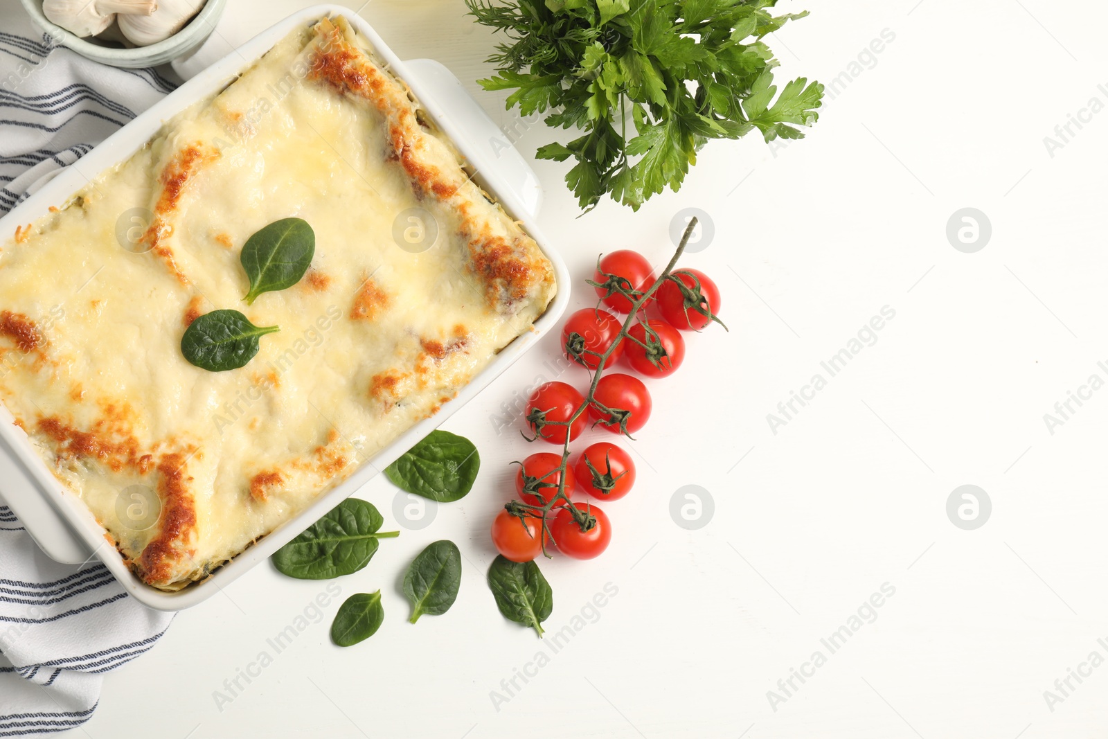 Photo of Delicious spinach lasagna in baking dish and ingredients on white table, flat lay. Space for text