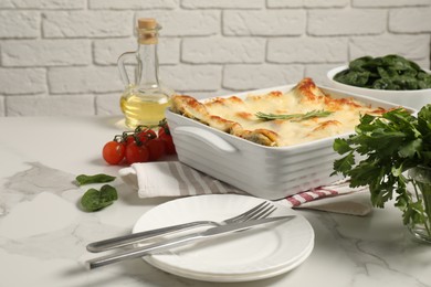 Photo of Delicious spinach lasagne in baking dish and ingredients on grey marble table