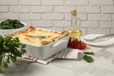 Photo of Delicious spinach lasagne in baking dish and ingredients on grey marble table