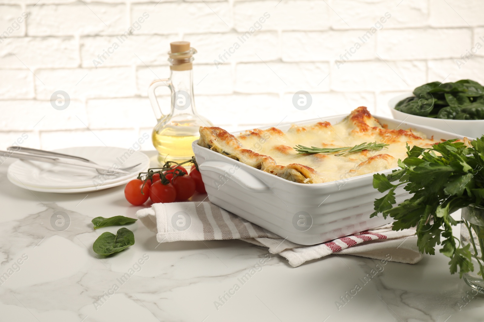 Photo of Delicious spinach lasagne in baking dish and ingredients on grey marble table