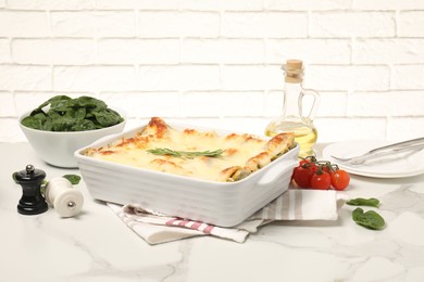 Photo of Delicious spinach lasagne in baking dish and ingredients on grey marble table