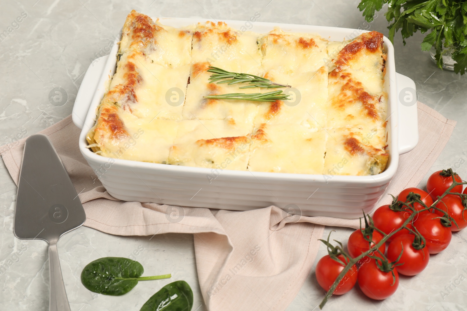 Photo of Delicious spinach lasagne in baking dish served on grey marble table