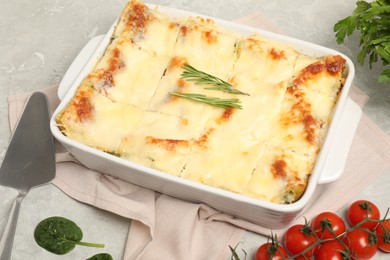 Photo of Delicious spinach lasagne in baking dish served on grey marble table