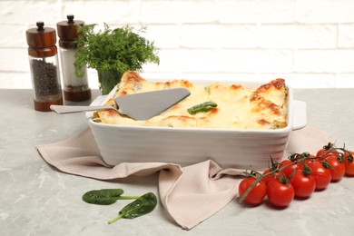 Photo of Delicious spinach lasagne in baking dish and ingredients on grey marble table