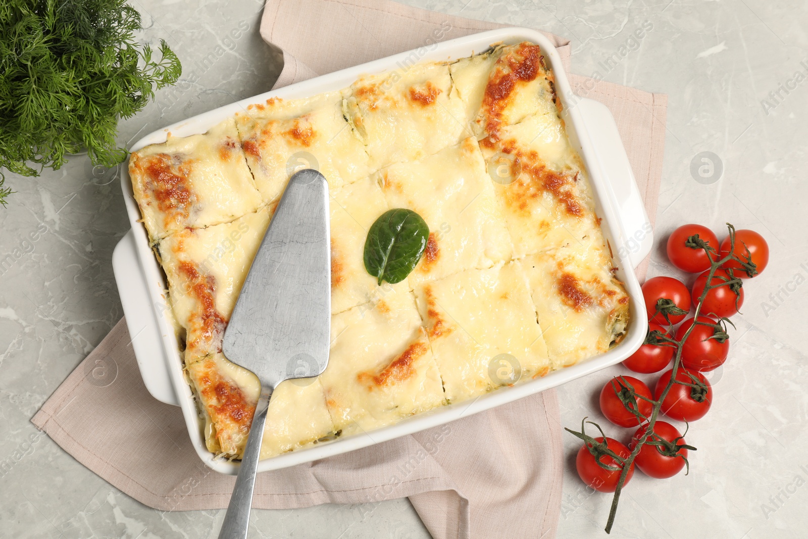 Photo of Delicious spinach lasagne in baking dish served on grey marble table, flat lay