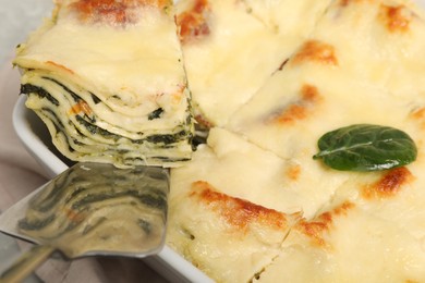 Photo of Taking piece of delicious spinach lasagne at table, closeup