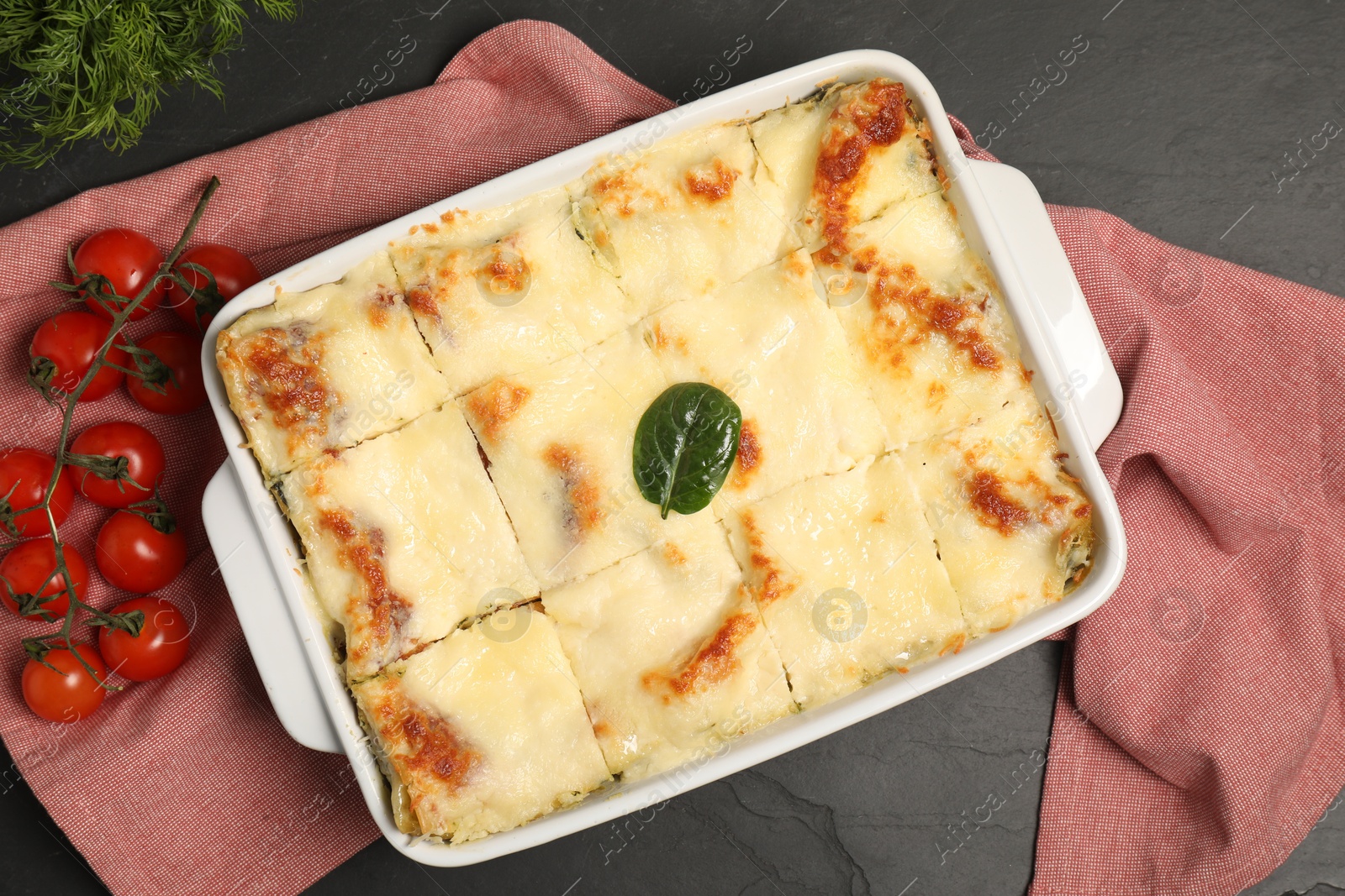 Photo of Delicious spinach lasagne in baking dish and ingredients on grey table, top view