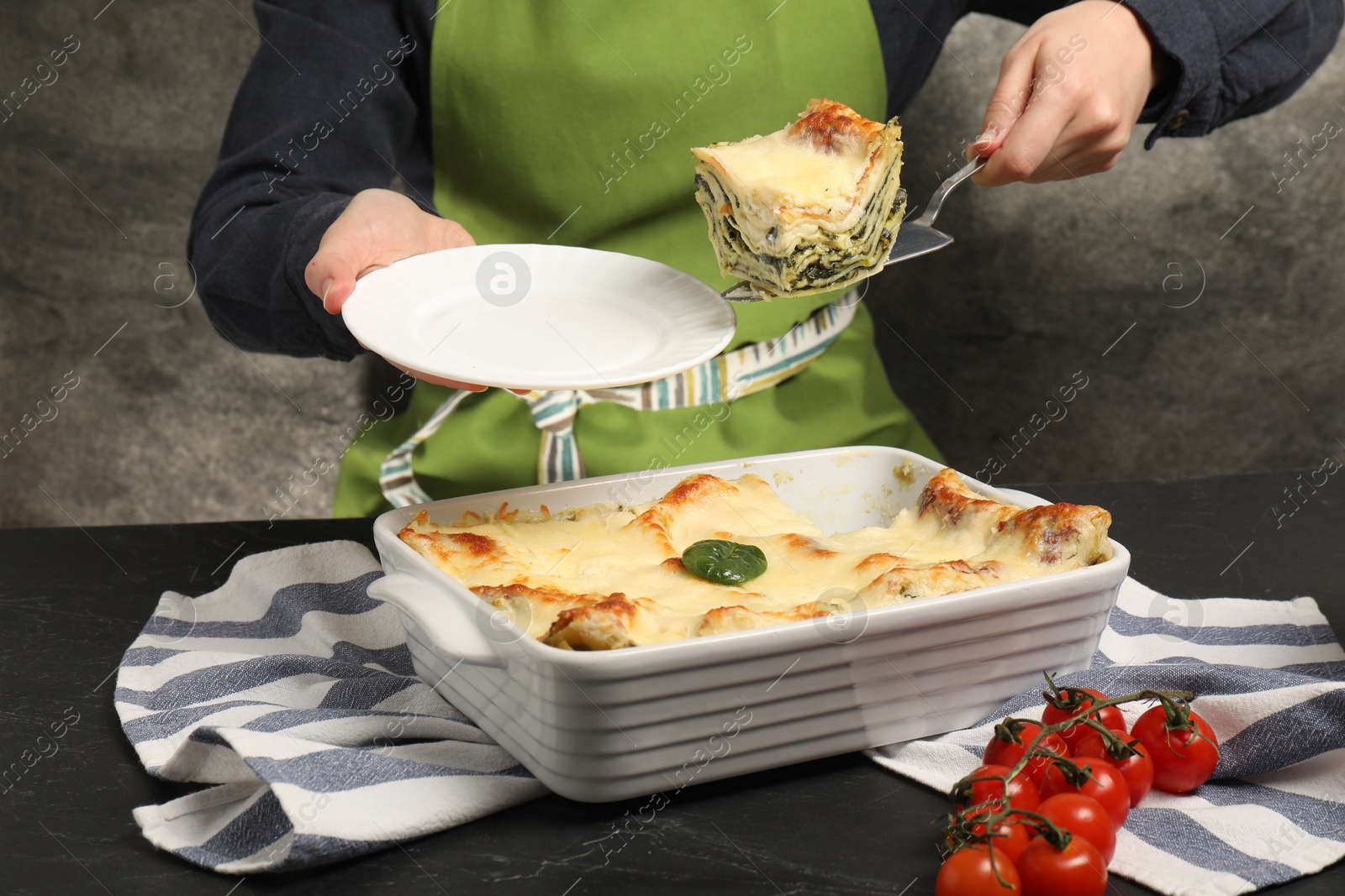 Photo of Woman taking piece of delicious spinach lasagne at grey table, closeup