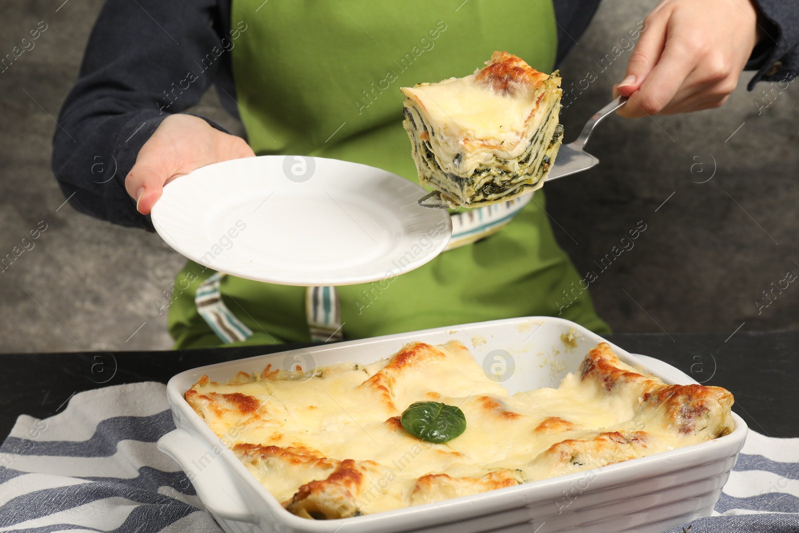 Photo of Woman taking piece of delicious spinach lasagne at grey table, closeup