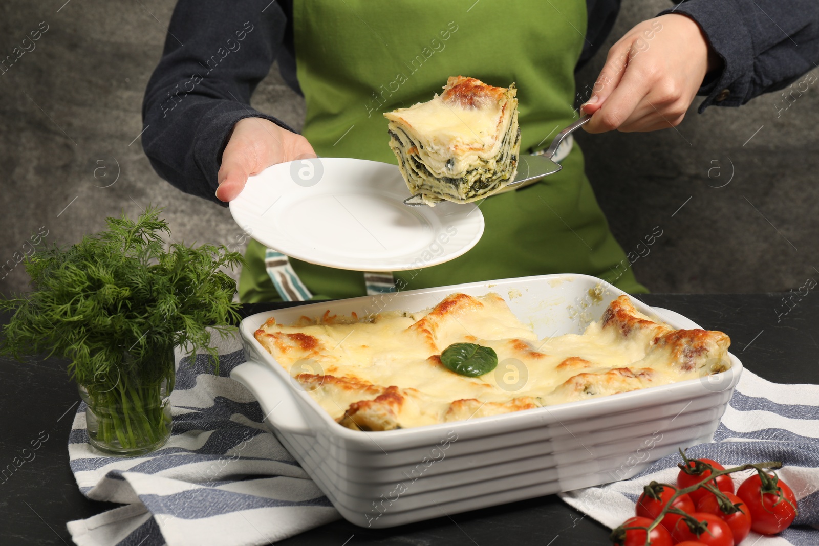 Photo of Woman taking piece of delicious spinach lasagne at grey table, closeup