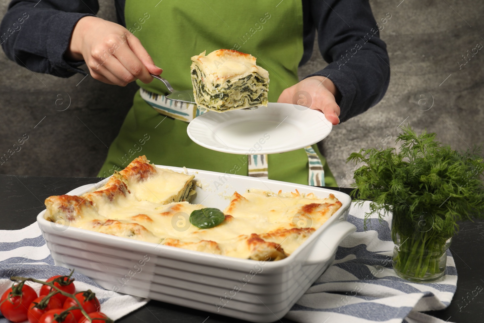 Photo of Woman taking piece of delicious spinach lasagne at grey table, closeup