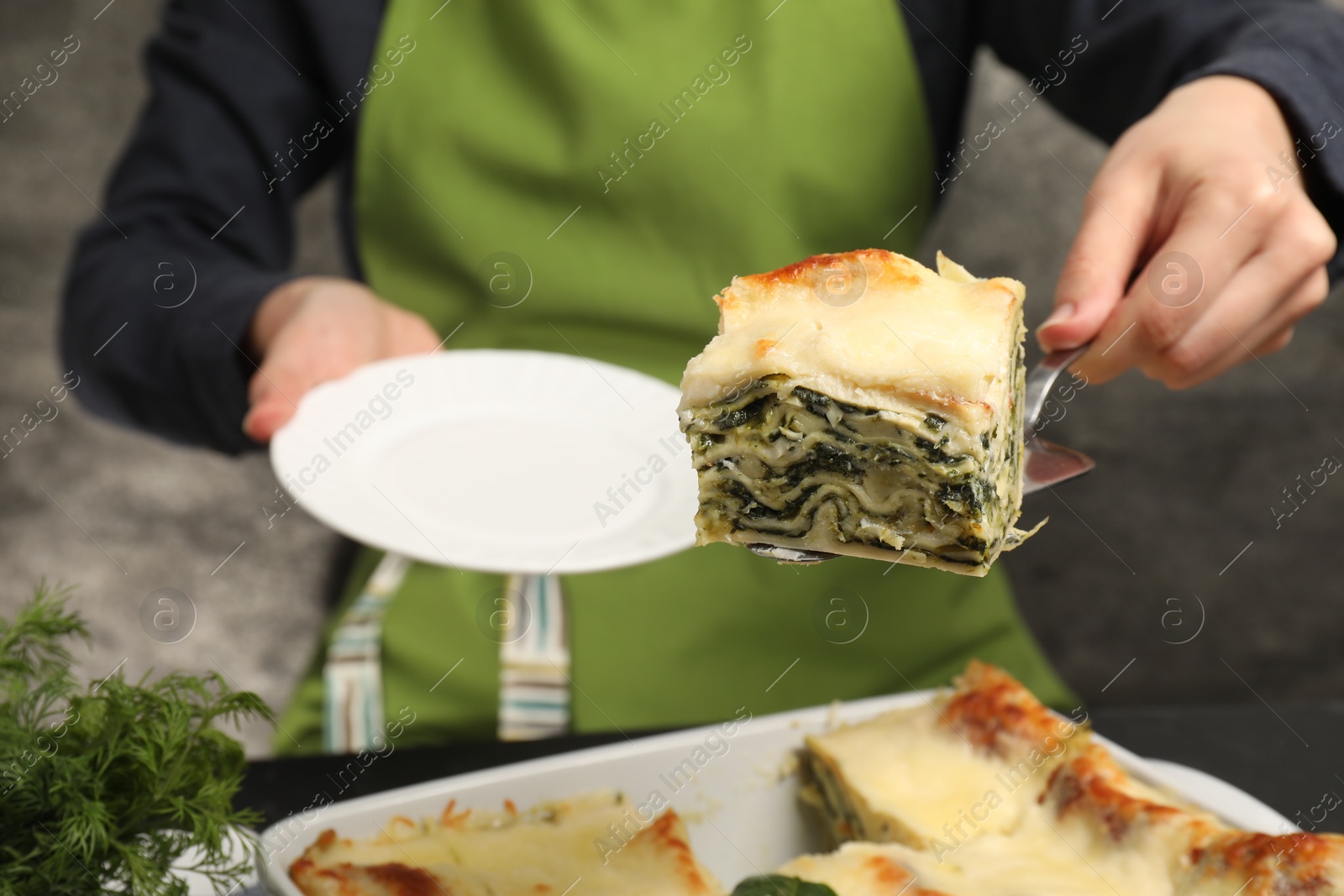 Photo of Woman taking piece of delicious spinach lasagne at grey table, closeup