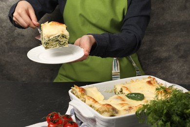 Photo of Woman taking piece of delicious spinach lasagne at grey table, closeup