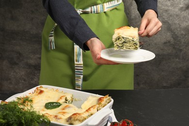 Photo of Woman taking piece of delicious spinach lasagne at grey table, closeup