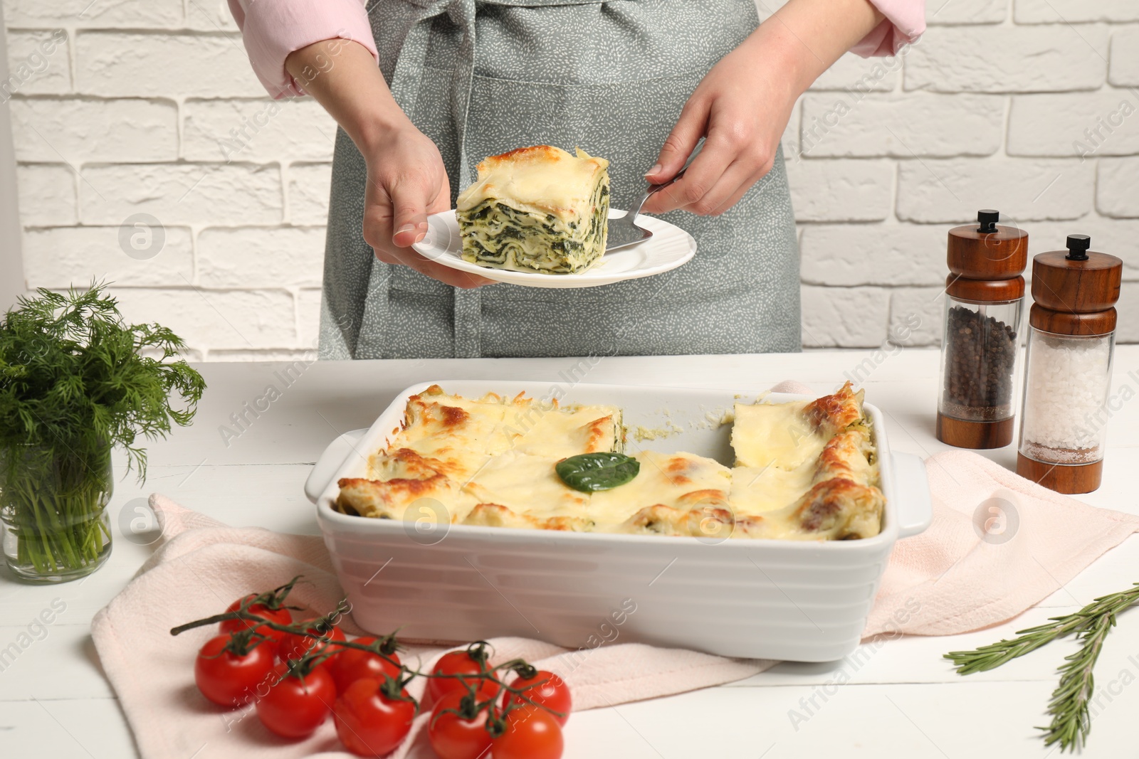 Photo of Woman taking piece of delicious spinach lasagne at white wooden table, closeup