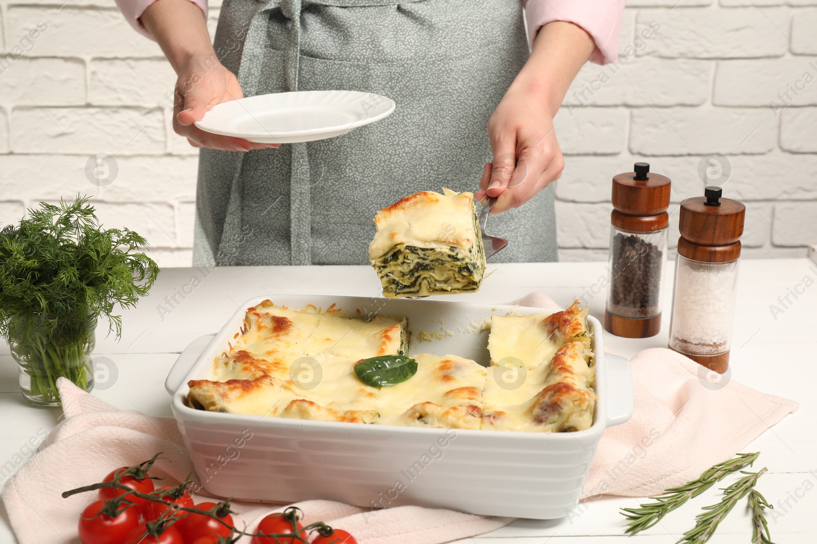 Photo of Woman taking piece of delicious spinach lasagne at white wooden table, closeup