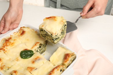 Photo of Woman taking piece of delicious spinach lasagne at white table, closeup