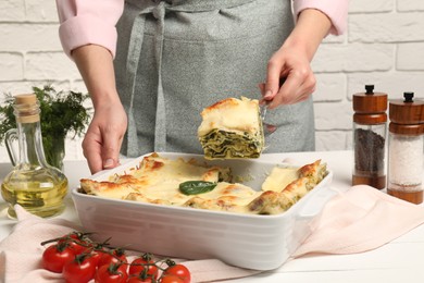 Photo of Woman taking piece of delicious spinach lasagne at white wooden table, closeup