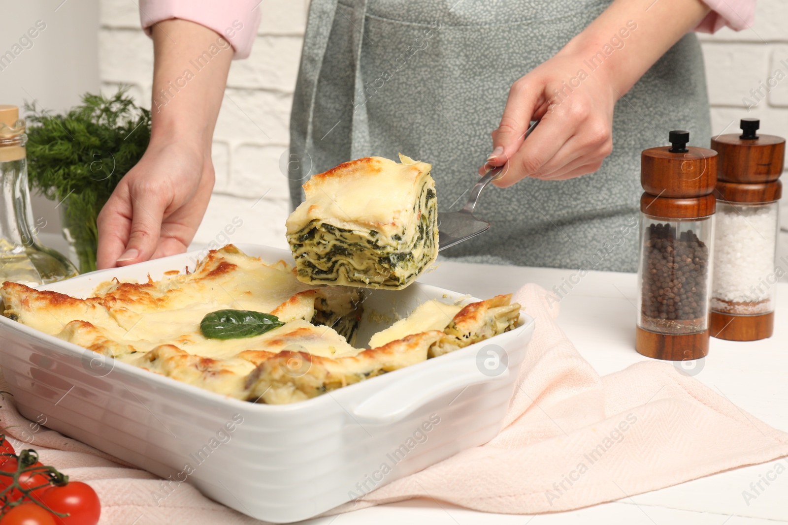 Photo of Woman taking piece of delicious spinach lasagne at white wooden table, closeup