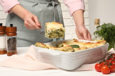 Photo of Woman taking piece of delicious spinach lasagne at white wooden table, closeup