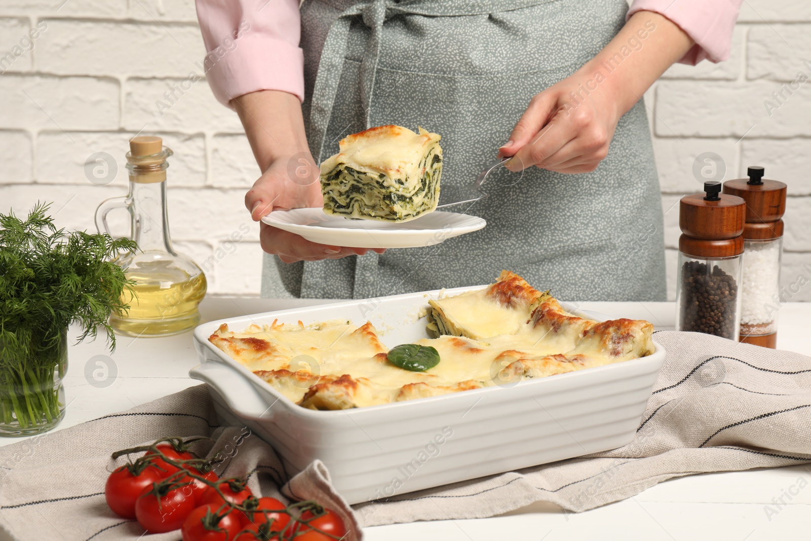 Photo of Woman taking piece of delicious spinach lasagne at white wooden table, closeup