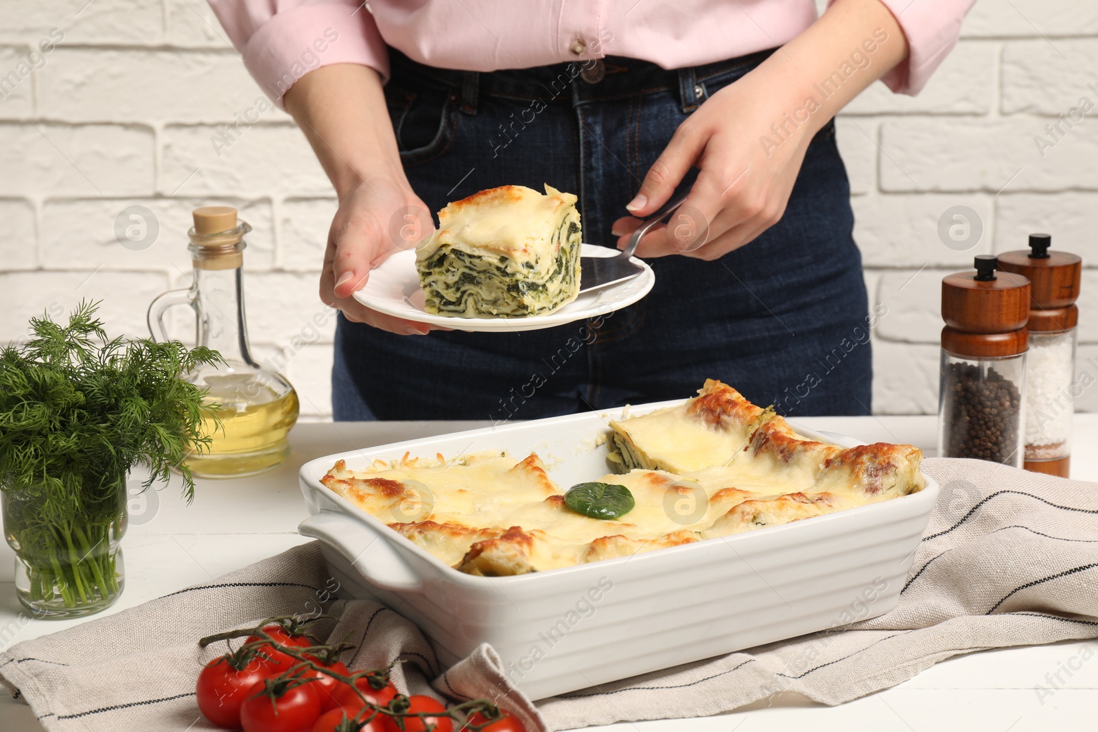 Photo of Woman taking piece of delicious spinach lasagne at white wooden table, closeup