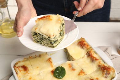 Photo of Woman taking piece of delicious spinach lasagne at white wooden table, closeup