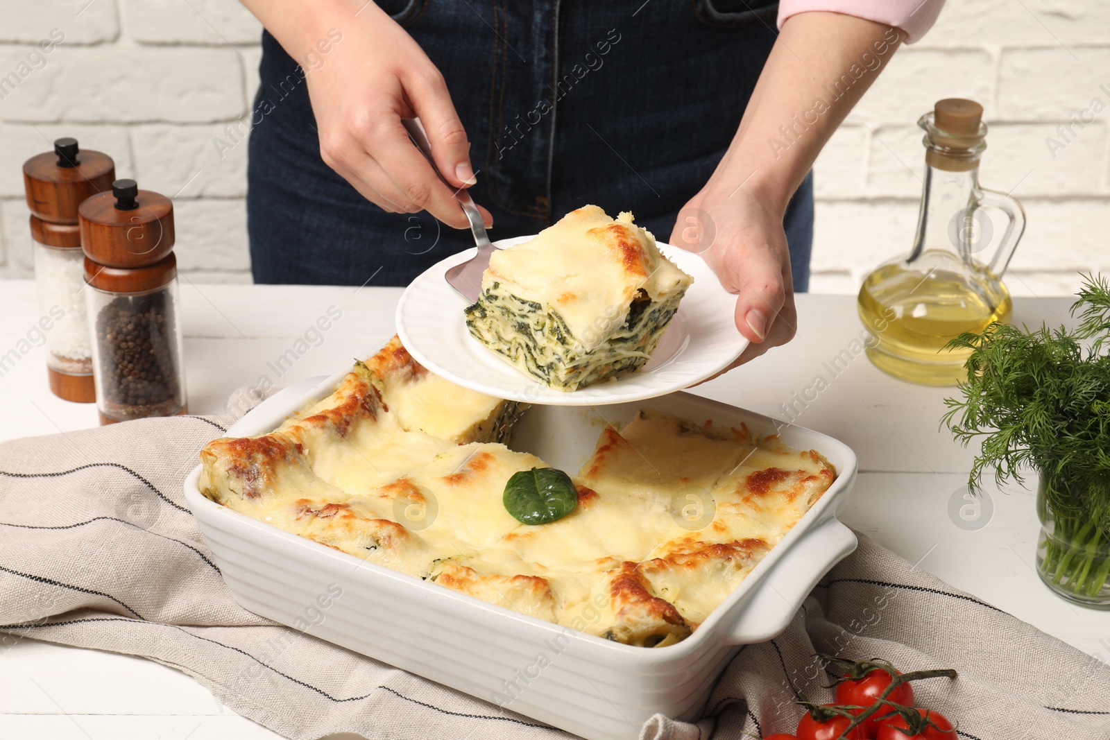 Photo of Woman taking piece of delicious spinach lasagne at white wooden table, closeup