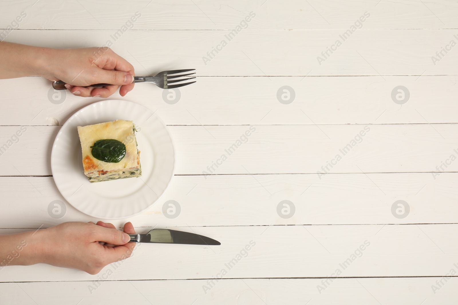 Photo of Woman with piece of delicious spinach lasagne at white wooden table, top view. Space for text