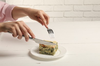 Photo of Woman eating piece of delicious spinach lasagne at white wooden table, closeup. Space for text