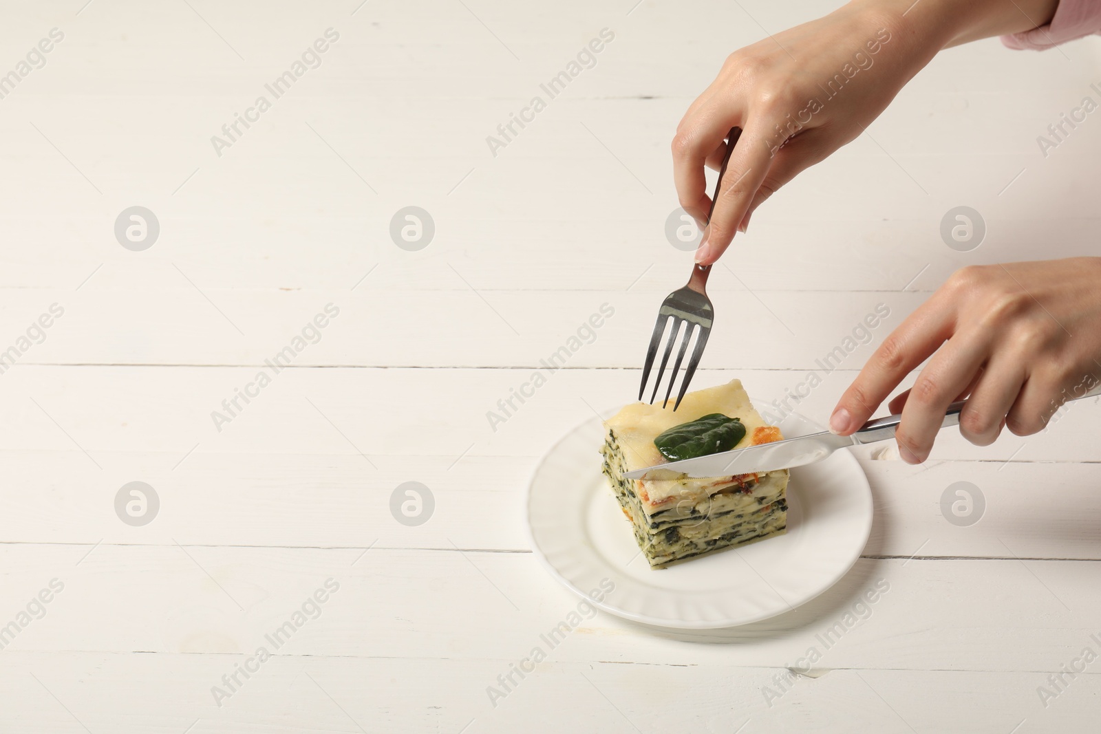 Photo of Woman eating piece of delicious spinach lasagne at white wooden table, closeup. Space for text