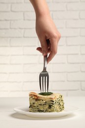 Photo of Woman eating piece of delicious spinach lasagne at white wooden table, closeup