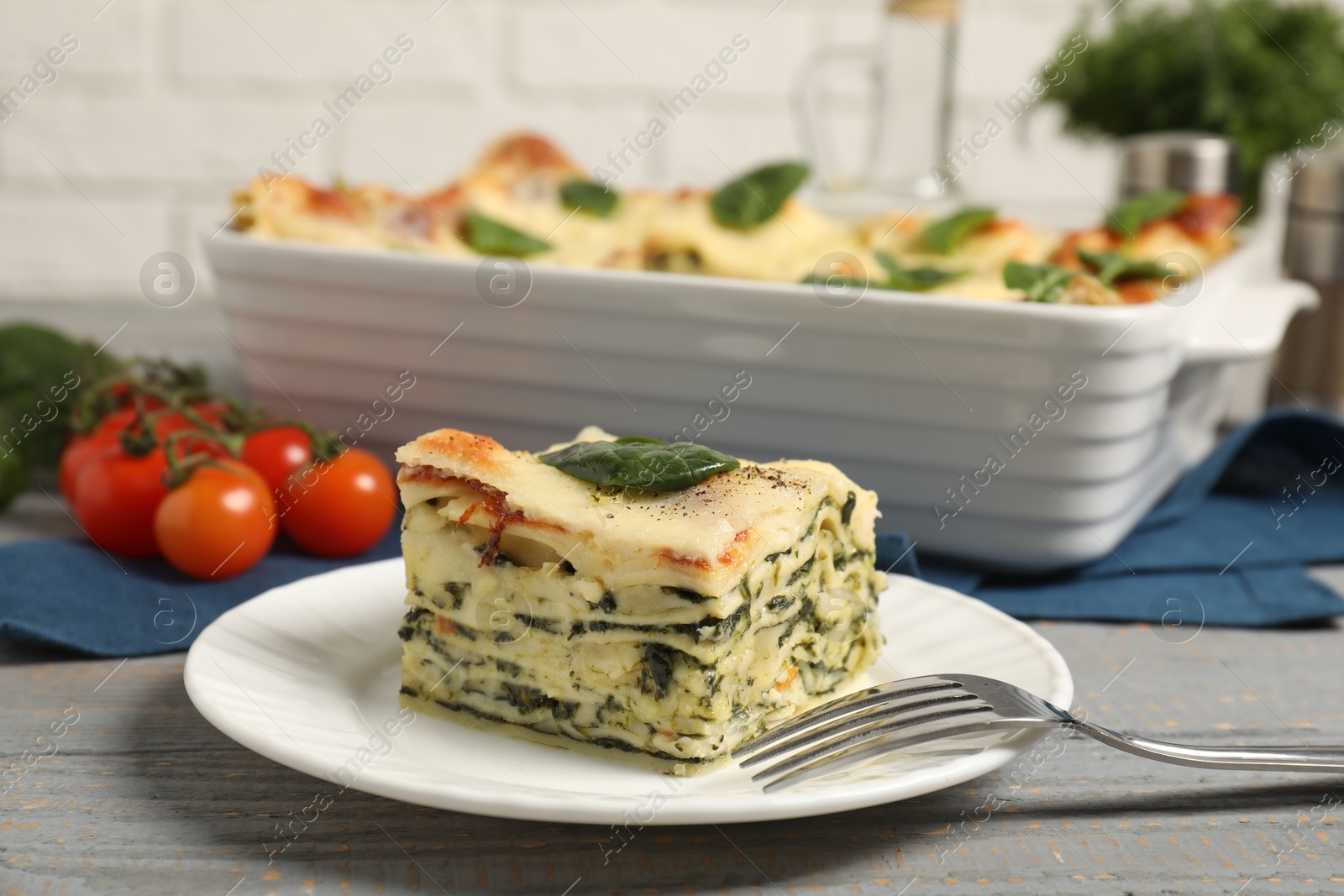 Photo of Piece of delicious spinach lasagne and fork on grey wooden table, closeup