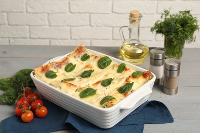 Photo of Delicious spinach lasagne in baking dish and ingredients on grey wooden table