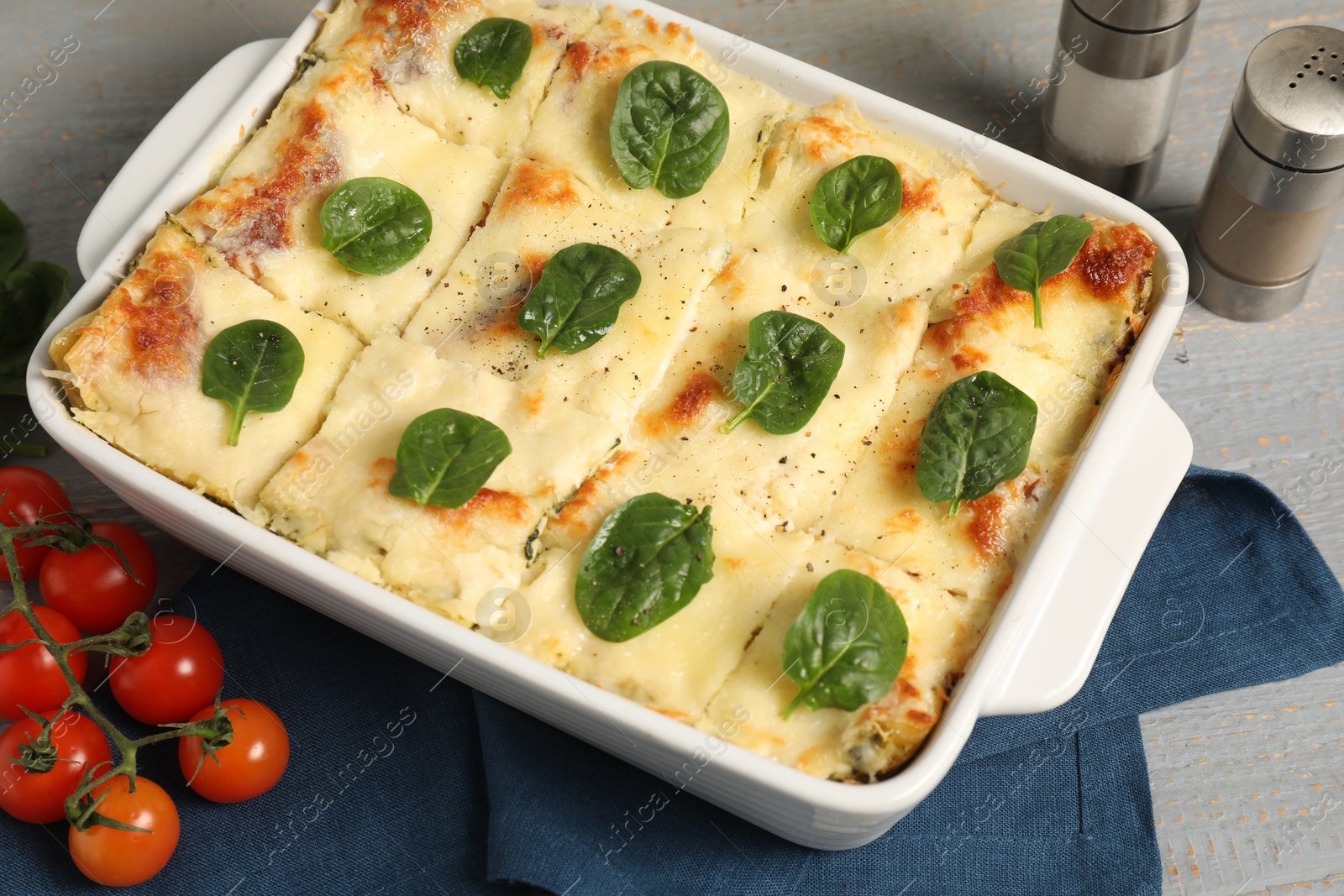 Photo of Delicious spinach lasagne in baking dish and ingredients on grey table