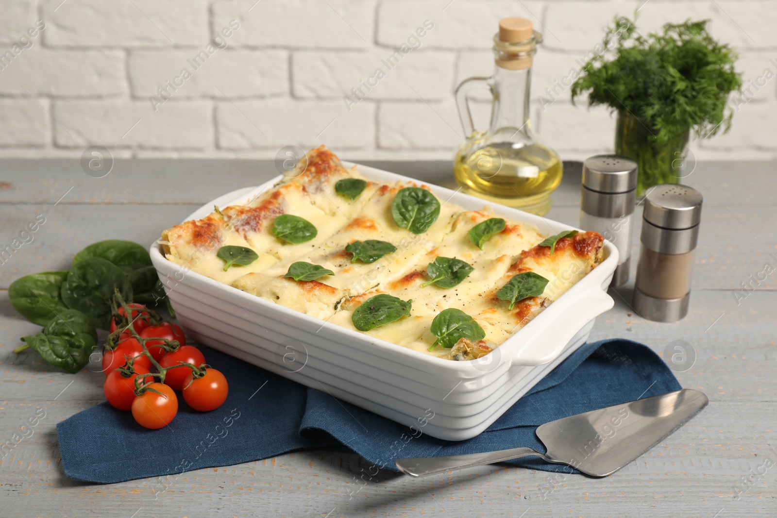 Photo of Delicious spinach lasagne in baking dish served on grey wooden table