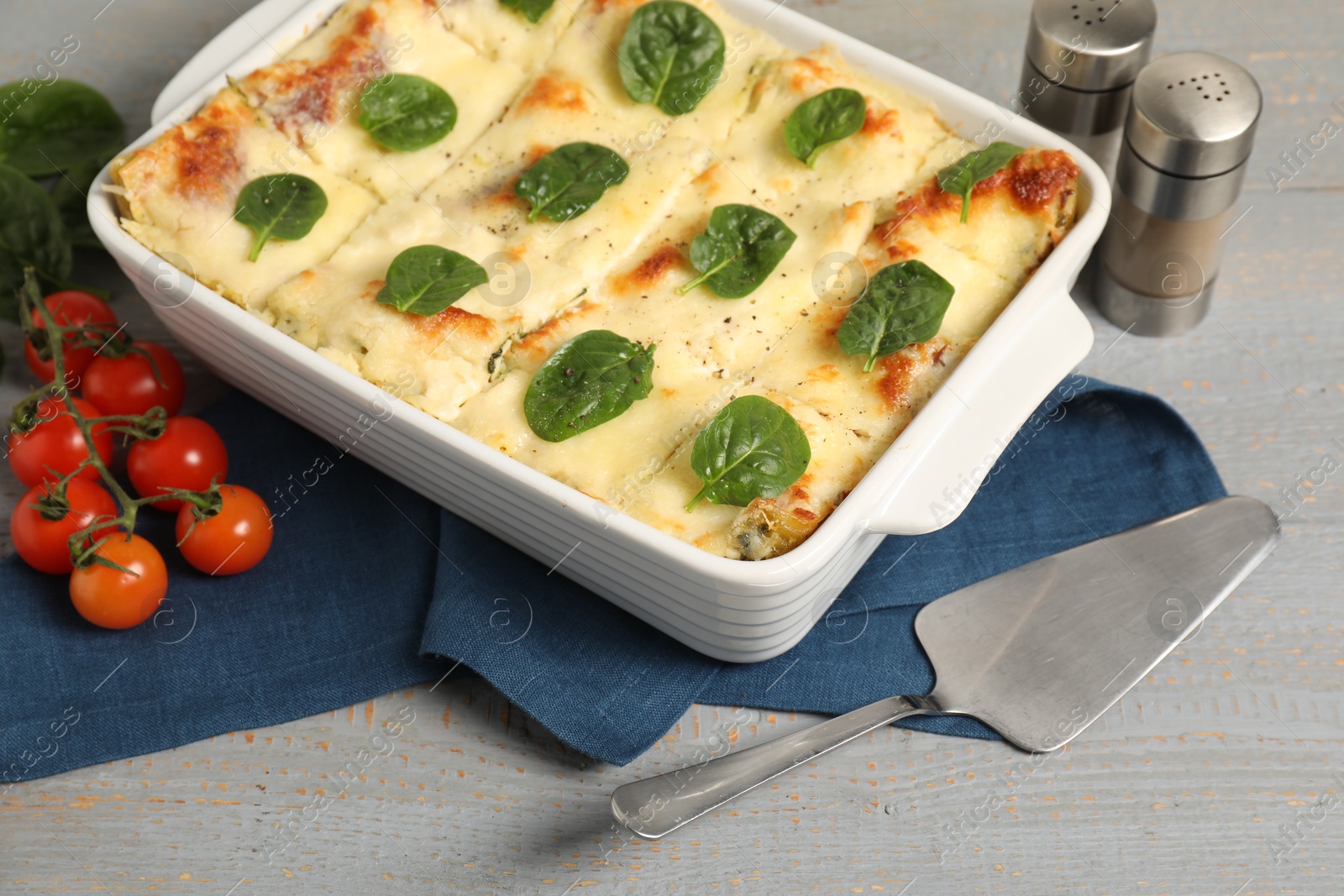 Photo of Delicious spinach lasagne in baking dish served on grey wooden table