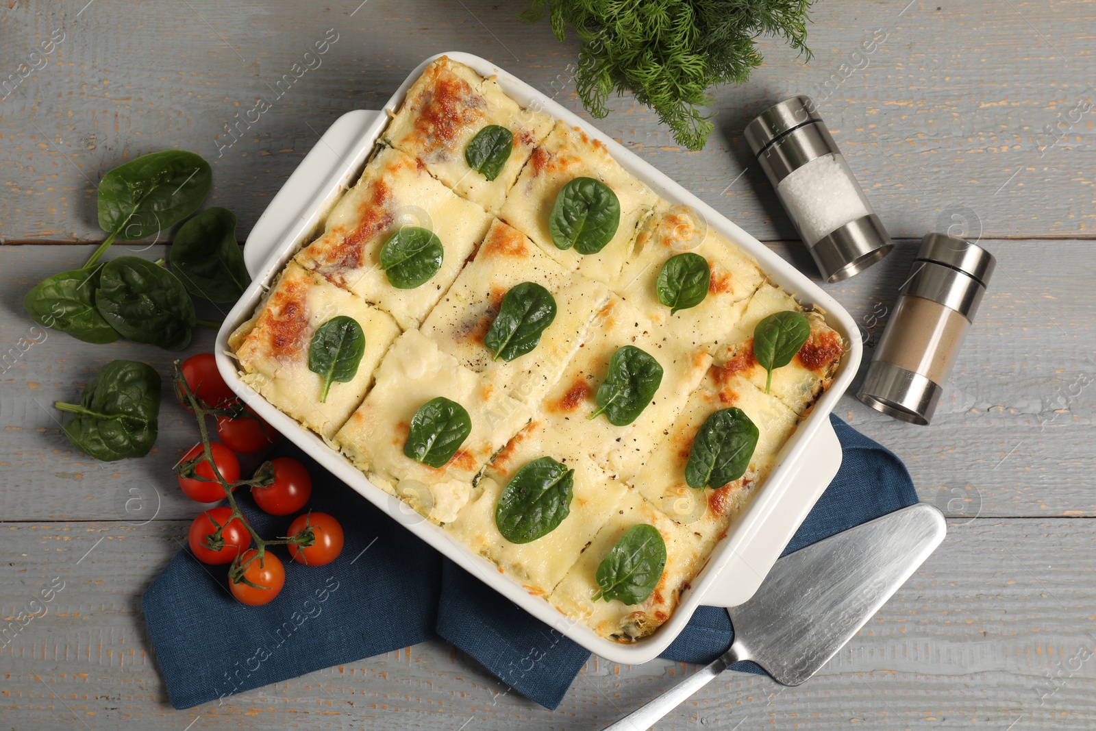 Photo of Delicious spinach lasagne in baking dish served on grey wooden table, flat lay