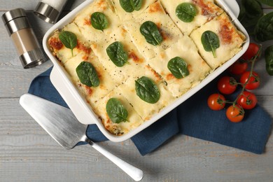 Photo of Delicious spinach lasagne in baking dish served on grey wooden table, flat lay