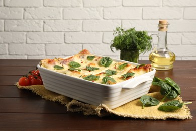 Photo of Delicious spinach lasagne in baking dish and ingredients on wooden table